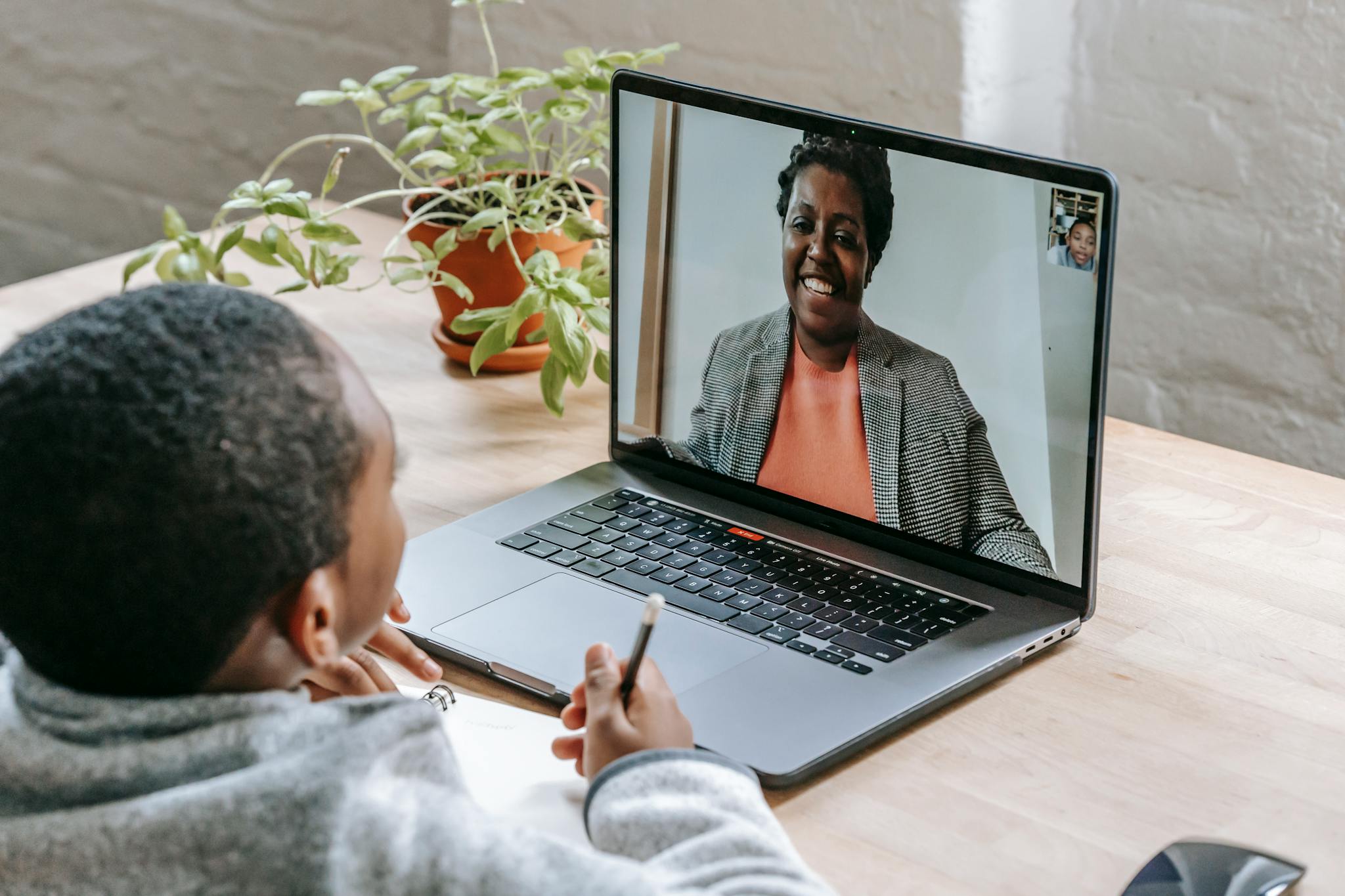A child participates in online tutoring, focusing on a laptop screen with a smiling tutor.