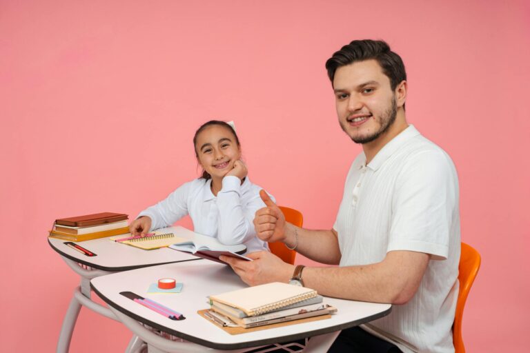 A teacher and a student smiling together at a desk in a classroom environment.