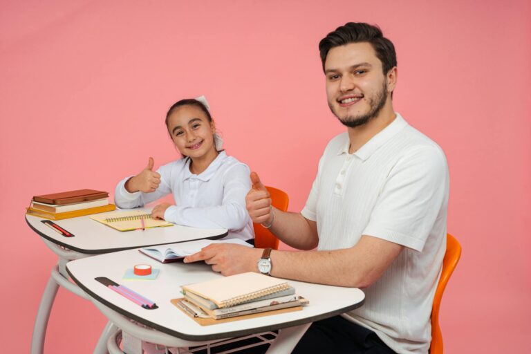 Smiling teacher and student at a desk, thumbs up, promoting education and positivity.